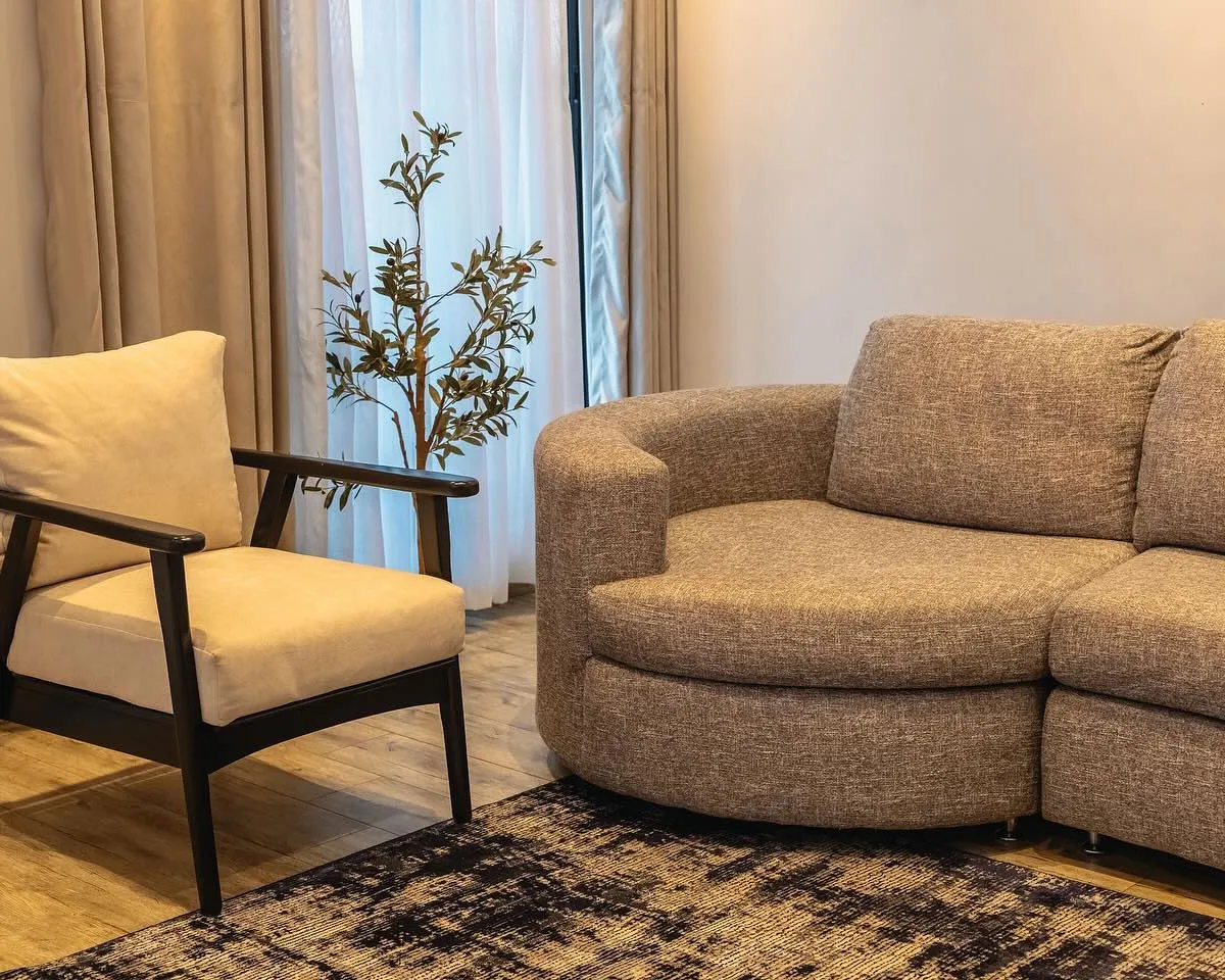 Curved upholstered sofa and a dark wood armchair by tall curtains