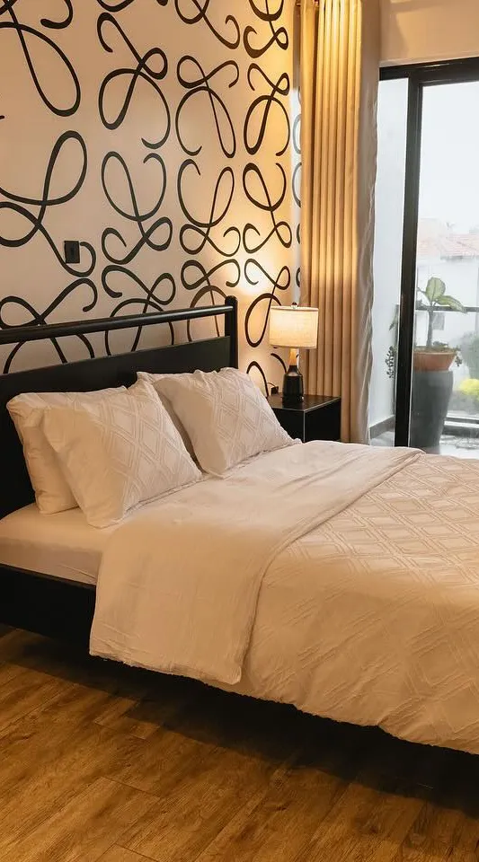 Black wooden bed and bedside tables in front of a patterned feature wall