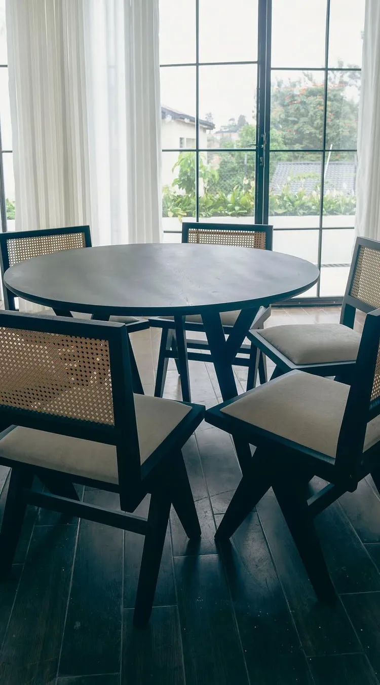 Round table with six black cane-back chairs by tall windows