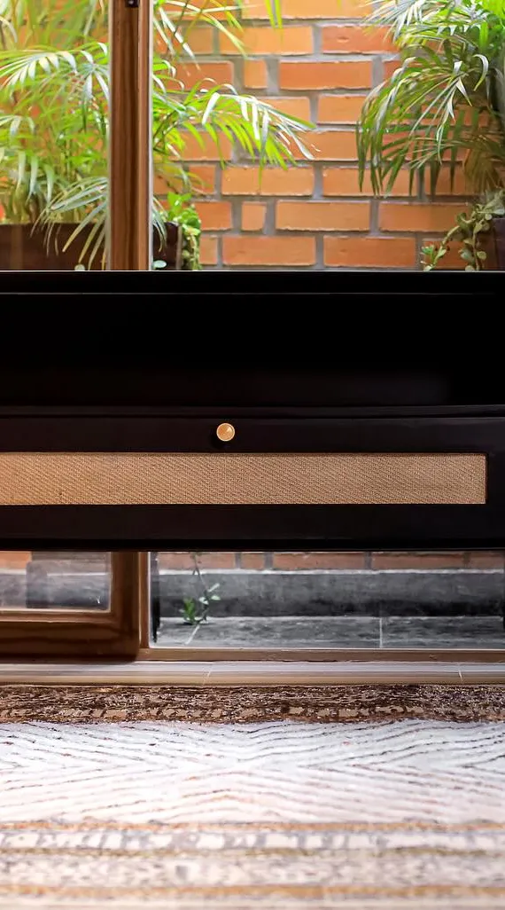 Black media unit with woven panels and brass knobs in front of a brick courtyard