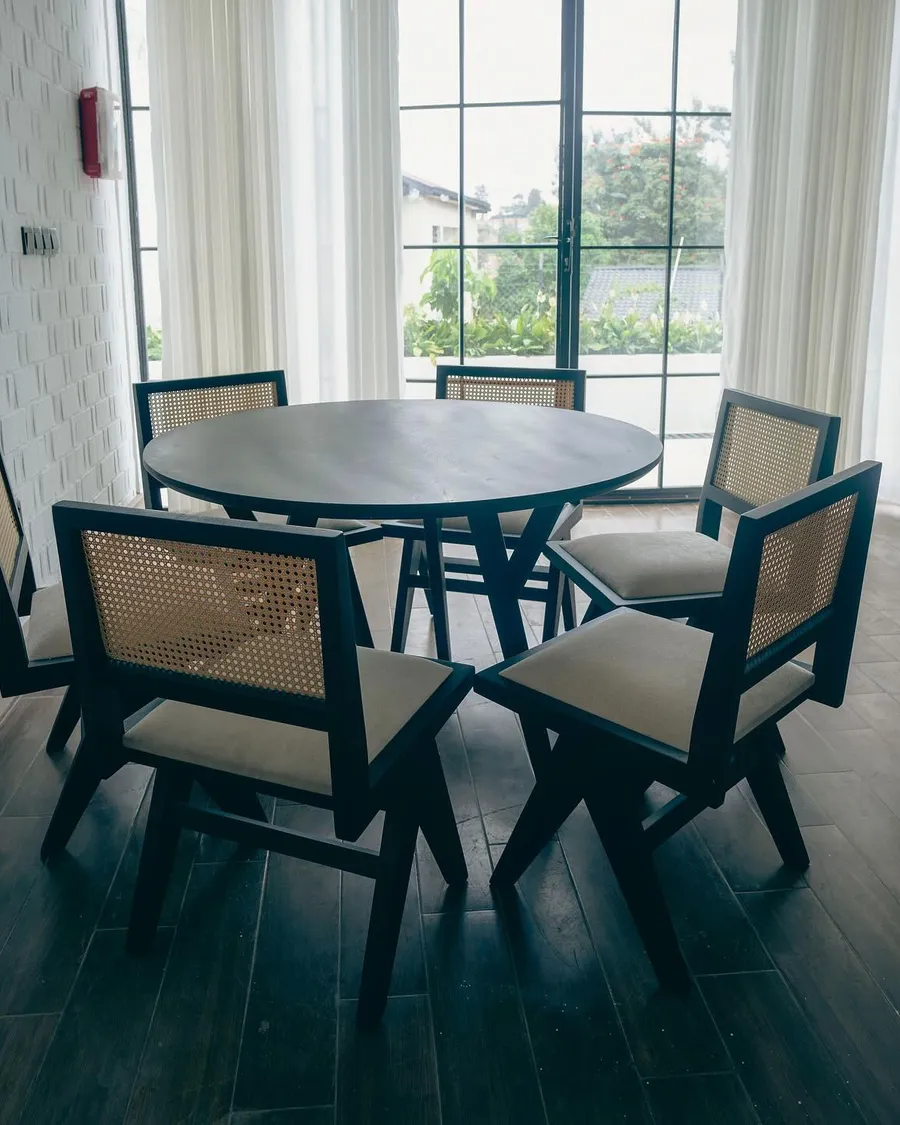 Round table with six black cane-back chairs by tall windows
