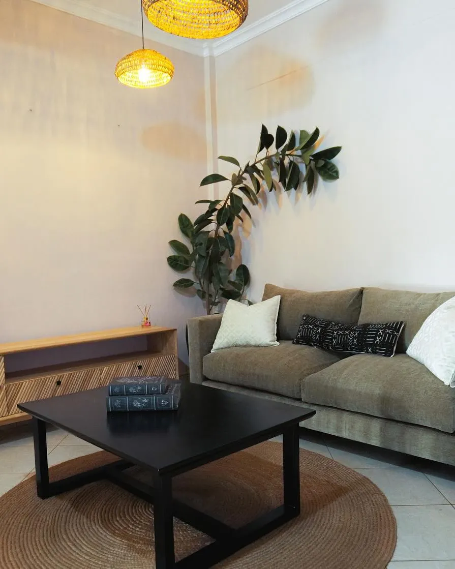 Olive sofa, black coffee table and a slatted media unit under rattan pendants