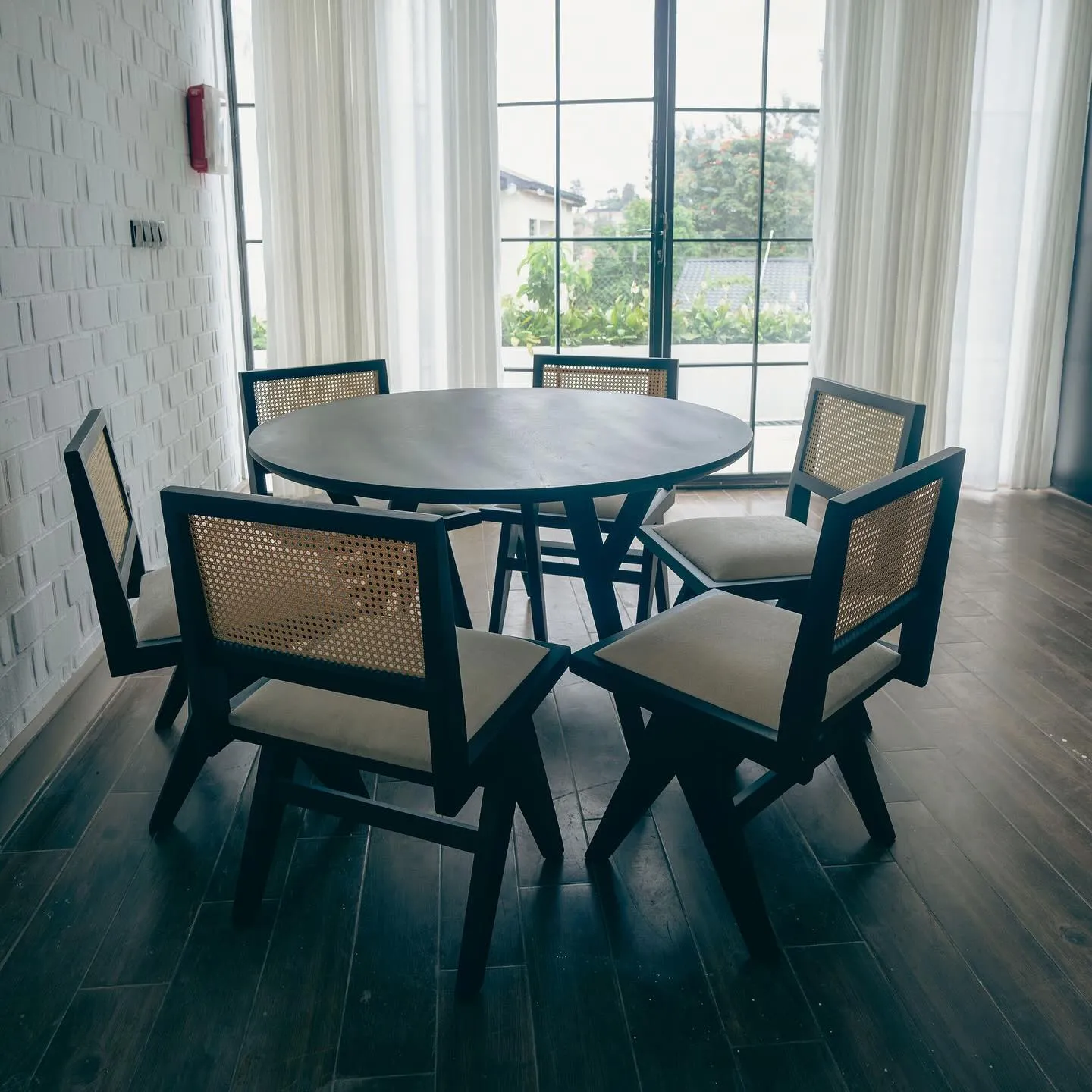 Round table with six black cane-back chairs by tall windows