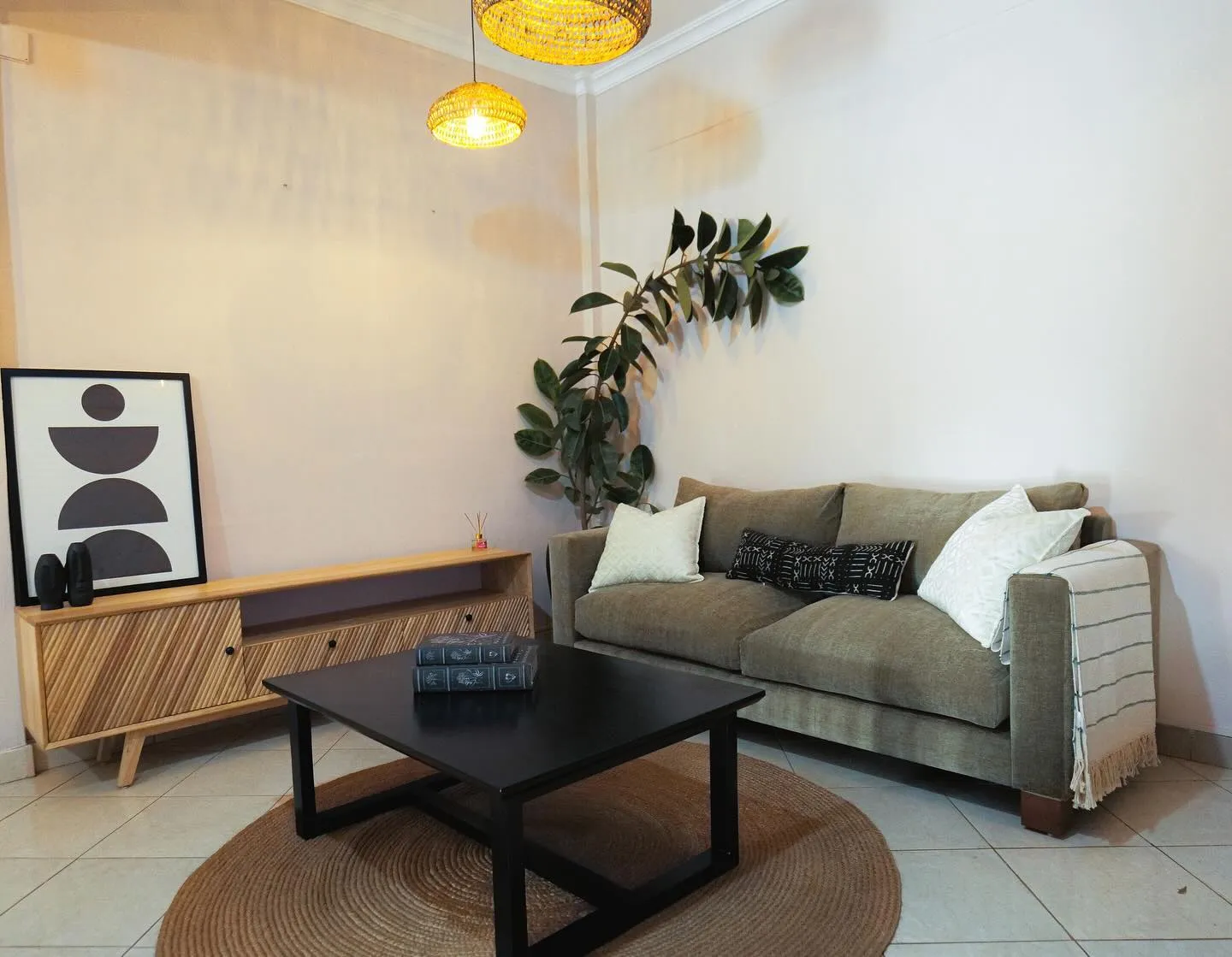 Olive sofa, black coffee table and a slatted media unit under rattan pendants
