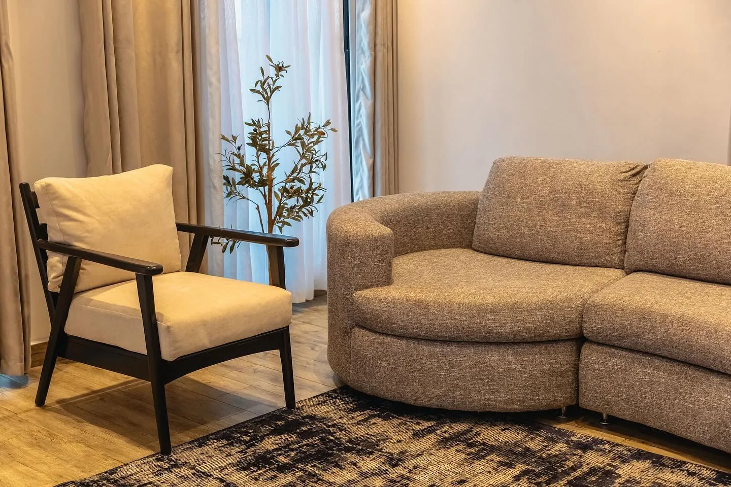 Curved upholstered sofa and a dark wood armchair by tall curtains